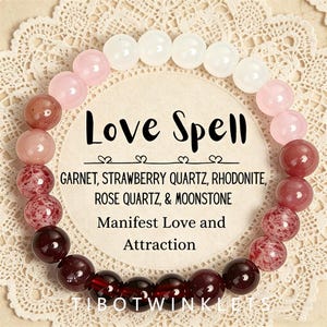 May include: A circular beaded bracelet featuring polished gemstones in shades of white, pale pink, deep red, and dark burgundy. The center card displays the text Love Spell, Garnet, Strawberry Quartz, Rhodonite, Rose Quartz, & Moonstone, Manifest Love and Attraction.