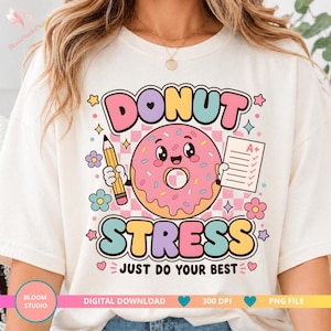 以下が含まれることがあります： クリーム色のTシャツにカラフルなグラフィック。グラフィックは、鉛筆とA+の成績の紙を持っているピンクのドーナツのキャラクターが特徴です。「DONUT STRESS」と「JUST DO YOUR BEST」の文字も表示されています。