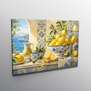 Op de afbeelding: Een wandkunstprint met een mediterrane scène met een blauw-witte betegelde richel met een gele kan, een kom met citroenen en een kom met olijven. Een uitzicht op de zee en bergen is zichtbaar door een boogvormige vensteropening.