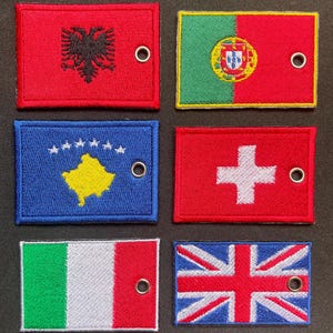Può includere: Toppe ricamate con bandiere nazionali: Albania, Portogallo, Kosovo, Svizzera, Italia e Regno Unito. Ogni toppa è rettangolare con un occhiello metallico. Le bandiere sono raffigurate nei loro colori e disegni ufficiali.