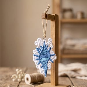 Può includere: Ornamento ricamato a forma di conchiglia nei toni del blu e del bianco, appeso a un espositore in legno. Il design intricato presenta un motivo dettagliato, perfetto per l'arredamento costiero o nautico. L'ornamento è sospeso da uno spago naturale.