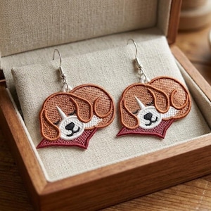 Könnte beinhalten: Gestickte Hundeohrringe mit silbernen Haken. Die Ohrringe zeigen ein braunes und weißes Hundegesicht mit rotem Kragen, präsentiert in einer Holzkiste mit beigem Stofffutter. Ein bezauberndes Accessoire.