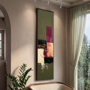 Può includere: Opera d'arte astratta da parete con cornice nera. L'opera presenta uno sfondo verde con blocchi rettangolari bordeaux, pesca, bianchi e neri. Un delicato disegno a linee bianche aggiunge dettagli. Il dipinto è esposto in una stanza con luce naturale.