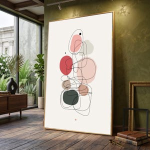 May include: Abstract art print with a gold frame, displaying a design of overlapping shapes and lines. The artwork features red, pink, grey, and black elements on a cream background. The framed print leans against a green wall.