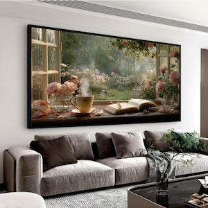 Puede incluir: Una obra de arte enmarcada representa una ventana con vistas a un jardín de rosas. Una taza de té humeante se encuentra junto a un libro abierto y rosas. La obra se exhibe sobre un sofá gris.