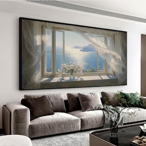 May include: A framed canvas print depicts a sunlit seascape viewed through an open window. White curtains billow in the breeze, and a vase of white flowers sits on the windowsill. The artwork is displayed above a gray sofa.