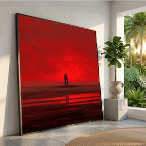 Könnte beinhalten: Großer gerahmter Kunstdruck mit einem Paar als Silhouette vor einem leuchtend roten Himmel. Das Kunstwerk zeigt eine romantische Szene mit einem feurigen Sonnenuntergang, der sich im Wasser spiegelt. Der Rahmen ist schwarz, und das Gesamtthema ist Liebe und Leidenschaft.