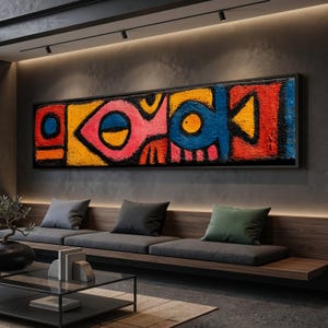 Könnte beinhalten: Abstraktes Kunstwerk in einem schwarzen Rahmen. Das Kunstwerk zeigt kräftige Formen und Farben, darunter Rot, Gelb, Blau und Orange. Das Design hat ein strukturiertes Aussehen mit einem schwarzen Rand. Es wird über einem Sitzbereich mit grauen Kissen angezeigt.