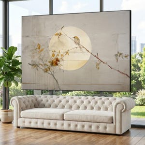 May include: Large framed artwork featuring a bird perched on a branch in front of a golden circle. The artwork has a neutral color palette with touches of gold and brown, and is displayed above a cream-colored tufted sofa.