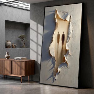 Könnte beinhalten: Großformatiges, gerahmtes abstraktes Kunstwerk mit einer zerrissenen, strukturierten Oberfläche, die zwei Schattenfiguren zeigt. Das Kunstwerk weist eine neutrale Farbpalette mit Weiß-, Beige- und Brauntönen auf, die ein Gefühl von Tiefe und Geheimnis erzeugt. Der Rahmen ist schwarz.