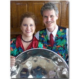 May include: A man and woman wearing colorful vests with tropical prints are holding a large silver steel pan drum. The text "Steel Baroque - Steel Pan Ensemble" is at the top of the image. The text "Catherine & Brett Wm. Templeton" is at the bottom of the image.