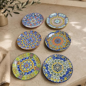 May include: A set of six round ceramic plates, each featuring a unique, intricate, and colorful mandala-inspired pattern. The designs incorporate vibrant shades of blue, yellow, green, and orange, arranged in symmetrical, detailed floral motifs.