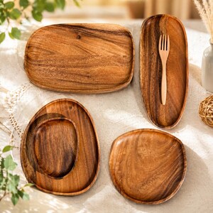 Puede incluir: Un conjunto de bandejas de madera y un tenedor de madera. Las bandejas tienen varias formas, incluyendo rectangular, ovalada y redonda, todas con un acabado de veta de madera natural. El tenedor está colocado en una de las bandejas ovaladas.