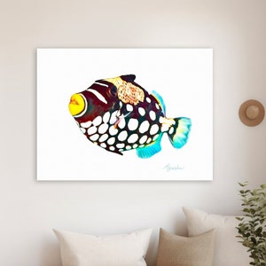 May include: A rectangular wall art print featuring a clown triggerfish with a dark body, white spots, a bright yellow mouth, and blue-tinted fins. The fish is depicted against a plain white background with a signature in the bottom right corner.