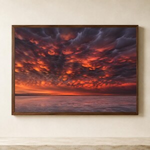 Könnte beinhalten: Ein rechteckiger Wandkunstdruck in einem dunklen Holzrahmen mit einer Landschaftsaufnahme eines Sonnenuntergangs über einem ruhigen Gewässer. Der Himmel ist mit strukturierten, dunkelvioletten und orangefarbenen Wolken gefüllt, die vom roten Licht der Sonne beleuchtet werden.