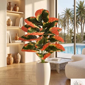Peut inclure: Une grande plante artificielle aux feuilles panachées dans des tons orange vif, vert foncé et jaune, placée dans un pot cylindrique blanc lisse. La plante présente de multiples feuilles larges en forme de cœur sur des tiges fines.