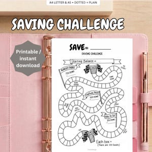 May include: A white paper saving challenge tracker with a black ink path of 100 boxes, featuring a start and finish line with checkered flags, motivational text, and labels for progress milestones, displayed inside a pink binder with a metal pen.