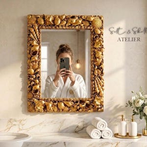 May include: A rectangular gold mirror with a seashell design frame. The mirror is in a bathroom setting, with a white sink, gold faucet, and decorative items. The text "Salt & Shell ATELIER" is visible.