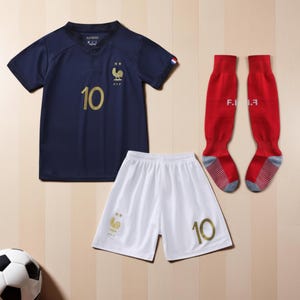 Pode incluir: Um conjunto de futebol azul marinho, incluindo uma camisa com o n&uacute;mero 10 dourado, cal&ccedil;&otilde;es brancos e meias vermelhas. A camisa apresenta um galo dourado e a bandeira francesa na manga.