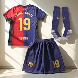 Op de afbeelding: Een complete voetbaltenueset met een shirt, shorts en sokken. Het shirt is rood en blauw met de naam "LAMINE YAMAL" en het nummer "19" in goud. De shorts en sokken zijn marineblauw met gouden details.