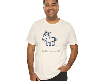 May include: A cream-colored short-sleeve t-shirt featuring a dark blue hand-drawn style illustration of a horse with large eyes. Below the illustration, the text reads "by Nigel, aged 62 1/2" in a dark blue cursive script font.