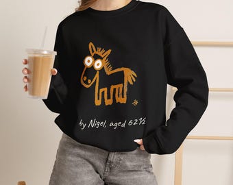 May include: A black long-sleeve sweatshirt featuring a gold-colored, hand-drawn style illustration of a horse with large eyes. Below the horse, the white text reads, "by Nigel, aged 62 1/2". The sweatshirt has a crew neckline and long sleeves.
