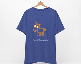 May include: A blue short-sleeve t-shirt featuring a brown line-art drawing of a horse with large white-rimmed eyes. Below the horse, the text reads "by Nigel, aged 62½" in a white handwritten font. The shirt is displayed on a wooden hanger.