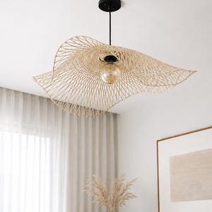May include: A pendant light fixture featuring a wide, wavy, natural-colored woven rattan shade with an open lattice pattern. The fixture is suspended by a black cord from a matching black ceiling canopy and includes a single exposed light bulb.