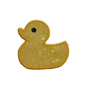 May include: A yellow rubber duck with a black eye, made of glittery fabric.