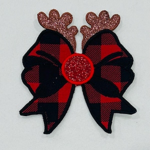 May include: A festive bow featuring a red and black check pattern, adorned with glittery brown reindeer antlers and a red glitter centre. Ideal for festive crafts, the bow is set against a white backdrop.