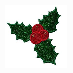 Puede incluir: Una hoja de acebo verde con purpurina y tres bayas rojas. La hoja de acebo es una decoración navideña tradicional.