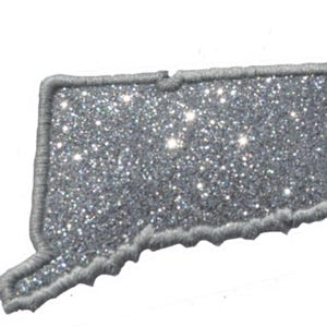 May include: A silver glitter embroidered patch in the shape of the state of Connecticut. The patch features a dense, sparkling silver surface texture and is finished with a thick, light gray stitched border that outlines the state's shape.