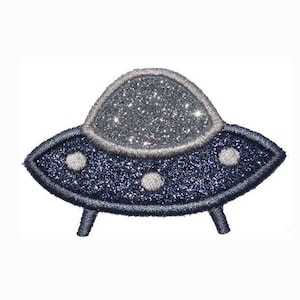 May include: An embroidered patch shaped like a flying saucer with a dark blue glittery main body, a silver glittery dome top, and three small silver circular accents along the base. The entire design is outlined with dark blue thread stitching.