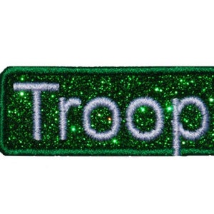 Puede incluir: Parche de hierro verde con purpurina con texto bordado en blanco que dice "Troop".