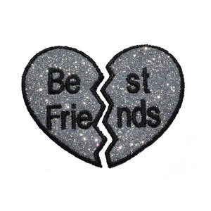 Pode incluir: Um remendo em forma de coração de glitter prateado é dividido ao meio com as palavras "Best Friends" escritas em preto.