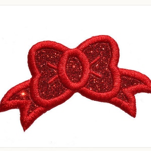 Puede incluir: Un lazo rojo con purpurina con un lazo central grande y dos lazos laterales más pequeños. El lazo está hecho de tela y tiene un acabado brillante.