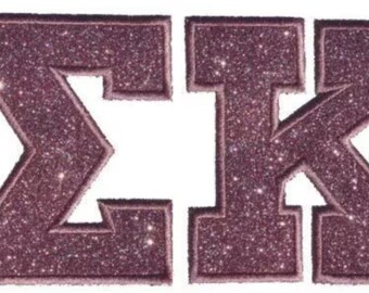 May include: Two embroidered Greek letters, Sigma and Kappa, featuring a dark mauve glitter finish. Each letter has a thick, stitched border in a matching mauve thread, creating a textured, raised appearance against a plain white background.