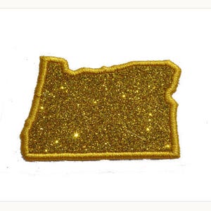 Puede incluir: Contorno de oro brillante del estado de Oregón. El contorno es un parche o una plancha.