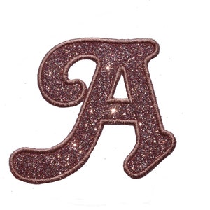 Könnte beinhalten: Ein dekorativer Aufnäher in Form des Buchstabens "A". Der Aufnäher hat eine tiefrosafarbene Farbe, ist mit Glitzer gefüllt und hat einen gestickten Rand. Der Schreibschriftbuchstabe ist zum Verzieren von Kleidung oder Accessoires gedacht. Der Glitzer fängt das Licht ein.