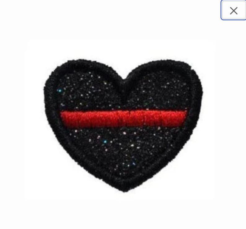 May include: Black heart-shaped patch with a red stripe across the center. The patch is covered in glitter.