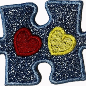May include: A blue glitter puzzle piece patch featuring a red heart and a yellow heart. The patch has a blue border and is set against a white background.