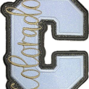 May include: A light blue letter "C" patch with a black and gold glitter border. The word "Sophie" is embroidered in gold cursive across the letter. The patch has a glittery, textured appearance.