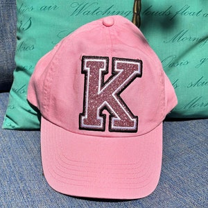 May include: Pink baseball cap with a large sparkly pink letter K on the front.