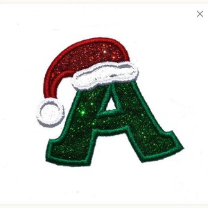 May include: Green glitter letter A with a red and white Santa hat on top.