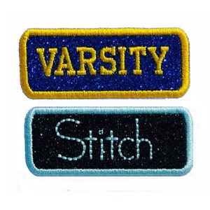 Può includere: Due toppe da stirare con glitter. La toppa superiore è blu con un bordo dorato e dice "VARSITY" in lettere gialle. La toppa inferiore è nera con un bordo blu chiaro e dice "Stitch" in lettere blu chiaro.