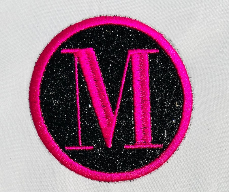 Puede incluir: Un c&iacute;rculo rosa con un fondo negro brillante y una letra M rosa en el centro.
