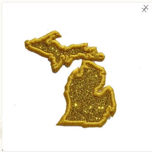 Pode incluir: Um contorno de purpurina dourada do estado de Michigan. O contorno é um remendo ou um ferro de passar.