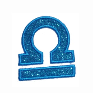 May include: A blue glitter iron-on patch with the astrological symbol for Libra.