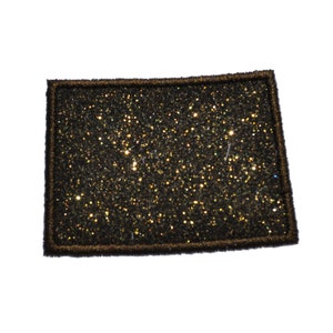 Op de afbeelding: Een strijkbare patch van gouden glitter met een zwarte omtrek. De patch is rechthoekig en heeft een glinsterend, textuurrijk oppervlak.