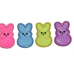 May include: Four colorful glitter bunny shaped iron-on patches. The bunnies are pink, blue, green, and purple.